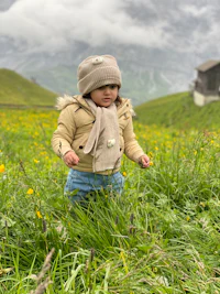 a little girl standing in a meadow with mountains in the background