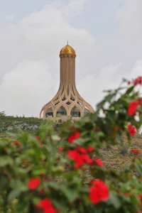 a golden tower sits on top of a hill with red flowers