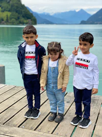 three children standing on a dock next to a lake