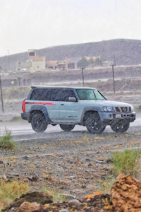 a gray suv driving on a dirt road in the rain